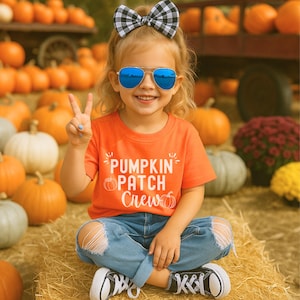 Puede incluir: Un niño lleva una camiseta naranja con el texto "Pumpkin Patch Crew", vaqueros azules y zapatillas deportivas blancas y negras. El niño lleva gafas de sol azules con espejo y un lazo a cuadros blanco y negro. El fondo presenta calabazas.