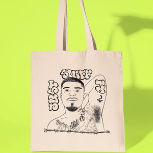 May include: A white canvas tote bag with a black and white illustration of a person's face with the words "Sniff" and "Hustle" written in a bubble font.