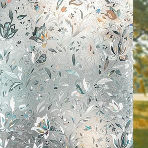 May include: A decorative window film with a floral pattern. The design features various flowers and leaves in shades of gray, white, teal, and brown. The film has a frosted appearance, creating a textured look. The overall theme is nature-inspired.