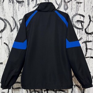 K&ouml;nnte beinhalten: Schwarze Jacke mit blauen Akzenten an Schultern und Oberarmen. Die Jacke hat einen hohen Kragen und einen durchgehenden Rei&szlig;verschluss. Das Material ist glatt, m&ouml;glicherweise wasserabweisend. Die Jacke ist f&uuml;r Outdoor-Aktivit&auml;ten konzipiert.