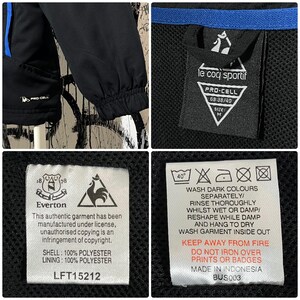 K&ouml;nnte beinhalten: Schwarze und blaue Sportjacke mit dem Logo "le coq sportif" und dem Etikett "Everton". Die Jacke hat ein "PRO-CELL"-Etikett und ein Gr&ouml;&szlig;enetikett M. Die Jacke besteht aus 100 % Polyester.