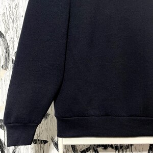 May include: A close-up of a navy blue sweatshirt. The image shows the sleeve and the lower portion of the garment, including the ribbed hem. The fabric appears to be a soft, knit material.