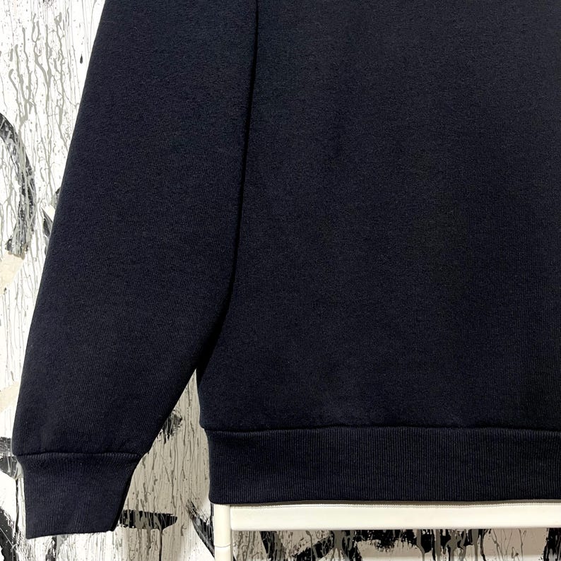 May include: A close-up of a navy blue sweatshirt. The image shows the sleeve and the lower portion of the garment, including the ribbed hem. The fabric appears to be a soft, knit material.