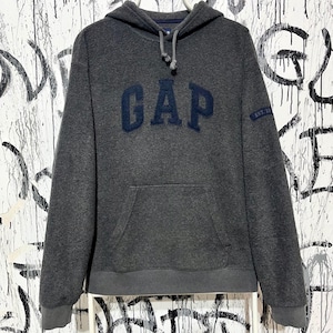 Puede incluir: Una sudadera con capucha gris carbón con un bolsillo delantero tipo canguro y una capucha con cordón. La palabra "GAP" está bordada en azul marino en el pecho. La manga tiene el texto "EST. 1969".