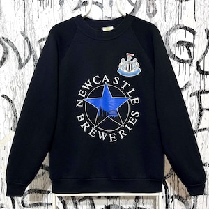 May include: Black crew neck sweatshirt with a blue star graphic and the words "Newcastle Breweries" in white. The sweatshirt also features a crest with a shield and the words "Newcastle United".