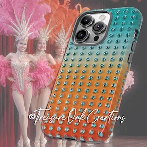 May include: A bedazzled phone case with a gradient of teal, orange, and yellow, adorned with numerous blue rhinestones. The case is shown in front of a stage with three women in pink costumes and feathered headdresses.