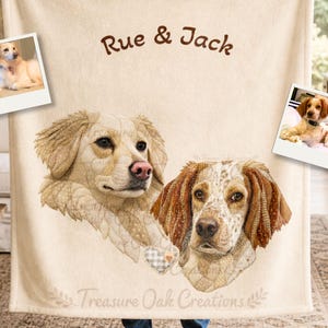 May include: A cream-colored blanket featuring a detailed illustration of two dogs, with the names "Rue & Jack" in brown script. The blanket also includes two small framed photos of dogs and the text "Treasure Oak Creations".