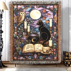 May include: A woven throw blanket featuring a stained glass style design with a black cat, an owl, a full moon, a cauldron, an open book, and lit candles. The rectangular blanket has a fringed border and displays a vibrant, multi-colored scene.