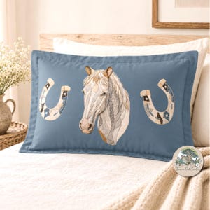 May include: A blue pillowcase featuring a detailed horse head and two horseshoes. The horse head is a patchwork design in shades of white, gray, and beige. The horseshoes have a patchwork design with stars and geometric patterns.
