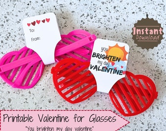 May include: Printable Valentine's Day card for glasses. The card features a red and white sun with the text "You brighten my day Valentine". The card is attached to a pair of red heart-shaped glasses.