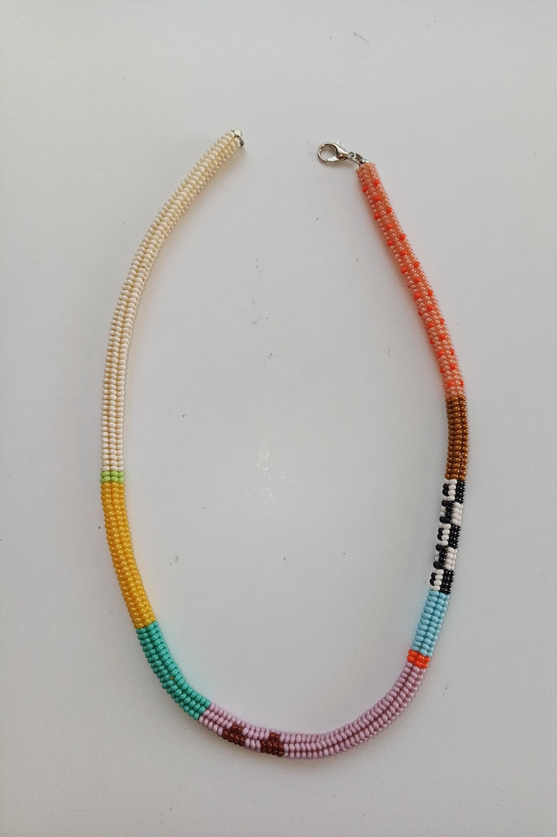 May include: A beaded necklace with a variety of colors. The necklace is made of small beads in sections of cream, yellow, teal, pink, brown, black, white, blue, orange, and coral. It has a silver clasp.