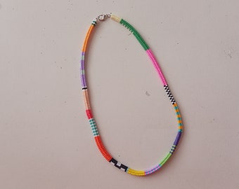 May include: A colorful beaded necklace with alternating stripes of orange, pink, green, purple, white, and black.