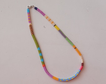May include: A colorful beaded necklace with a silver clasp. The necklace is made with small beads in shades of pink, green, blue, yellow, orange, and brown.