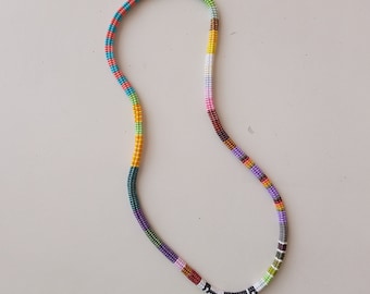 May include: A colorful beaded necklace with a variety of colors including red, orange, yellow, green, blue, purple, and brown. The necklace is made of small beads that are strung together in a repeating pattern.