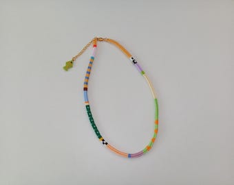 May include: A colorful beaded necklace with a gold-tone chain and a small green fish charm. The necklace features a variety of colors, including green, orange, blue, and purple, arranged in a striped pattern.