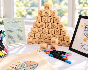 May include: A pyramid of light-colored wooden blocks featuring engraved animal illustrations, colors, and words. A sign reads Guest Instructions and Message Ideas for Baby. A canvas bag with a floral carriage print and markers are nearby.