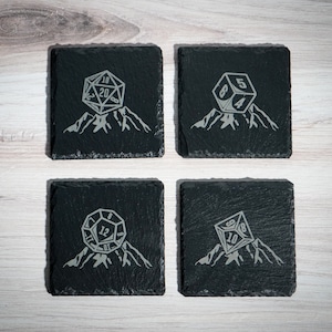 May include: Set of four black slate coasters with a white mountain and a 20-sided die design. The die shows different numbers on each coaster.