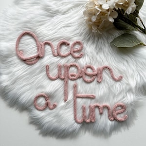 May include: Pink yarn letters spelling "Once upon a time" on a white fluffy surface.