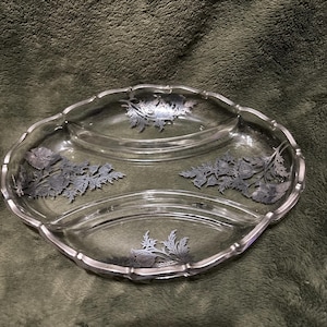 May include: A clear glass serving dish with a silver-colored rim and floral designs. The dish is divided into three sections and has a scalloped edge. The floral designs are in a silver color.