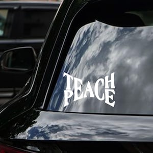 May include: White vinyl decal with the words "Teach Peace" in a retro font, applied to the rear window of a black car.