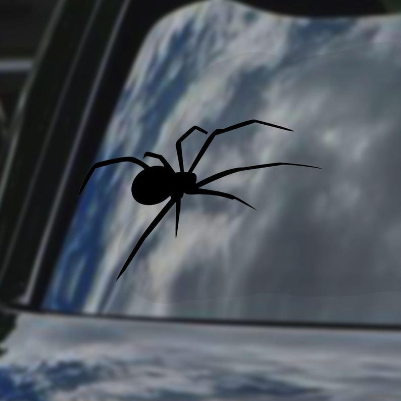 May include: A black spider silhouette decal, with eight legs and a rounded body, is affixed to a car window. The background shows a blurred view of a cloudy sky, creating a contrast between the dark spider and the lighter backdrop.