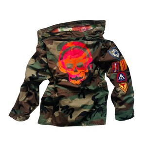 May include: Camouflage jacket with a pink and orange skull graphic and the text "Let the dogs out." The jacket has several patches on the sleeve, including a star, a red, white, and blue patch, and a patch with the letter "A" on it.