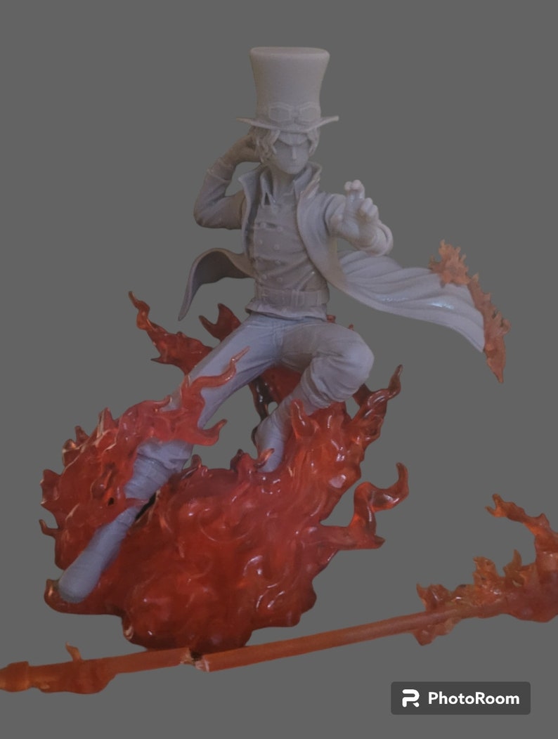 Pu&ograve; includere: Una statuetta grigia e bianca di un personaggio che indossa un cappello a cilindro e un lungo mantello, in piedi su una base di fiamme rosse. La statuetta &egrave; in posa in una posa d'azione dinamica, con una gamba sollevata e l'altra piegata. Il viso del personaggio &egrave; oscurato dal cappello.