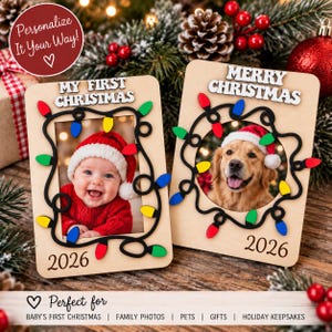 May include: Two rectangular wooden photo frames with rounded corners. The left frame features the text "MY FIRST CHRISTMAS" and "2026" with a black wire design and colorful light bulbs. The right frame features "MERRY CHRISTMAS" and "2026".