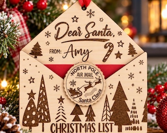 Puede incluir: Un adorno navideño de madera clara con forma de sobre que presenta el texto grabado Dear Santa, FROM: Amy, y CHRISTMAS LIST. Un sello circular de North Pole Air Mail con un gráfico de un trineo de renos está centrado en la solapa del sobre.