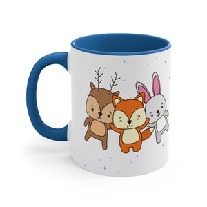 May include: White ceramic mug with a blue rim. The mug features a cartoon illustration of a deer, fox, and rabbit with blue stars on a white background.