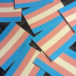 May include: A stack of transgender pride flag stickers. The stickers are blue, pink, and white.