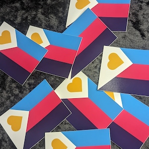 May include: Multiple stickers featuring a pride flag with a white triangle, a yellow heart, and horizontal stripes of purple, pink, blue, and light blue.