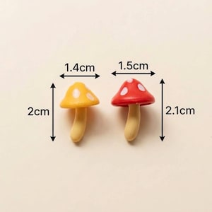 May include: Two miniature mushroom figurines with light beige stems and spotted caps. The yellow mushroom measures 1.4 cm wide by 2 cm tall. The red mushroom measures 1.5 cm wide by 2.1 cm tall. Both feature white spots on their rounded caps.
