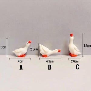 May include: Three white goose figurines with orange beaks and feet in different poses labeled A, B, and C. Goose A is 3.3 cm tall and 4 cm wide. Goose B is 2.5 cm tall and 4.3 cm wide. Goose C is 4.6 cm tall and 2.6 cm wide.