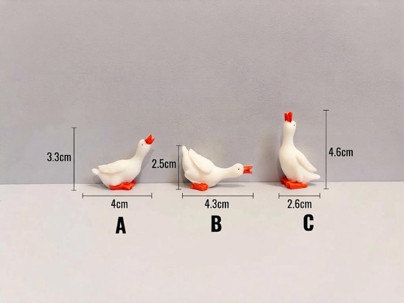 May include: Three white goose figurines with orange beaks and feet in different poses labeled A, B, and C. Goose A is 3.3 cm tall and 4 cm wide. Goose B is 2.5 cm tall and 4.3 cm wide. Goose C is 4.6 cm tall and 2.6 cm wide.