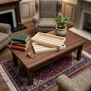 Peut inclure: Deux plateaux rectangulaires en bois clair avec des bases à lattes sont empilés sur une table basse en bois foncé. À côté des plateaux se trouve une petite pile de trois livres miniatures aux couvertures vertes et brunes et une bande de cuir pliée.