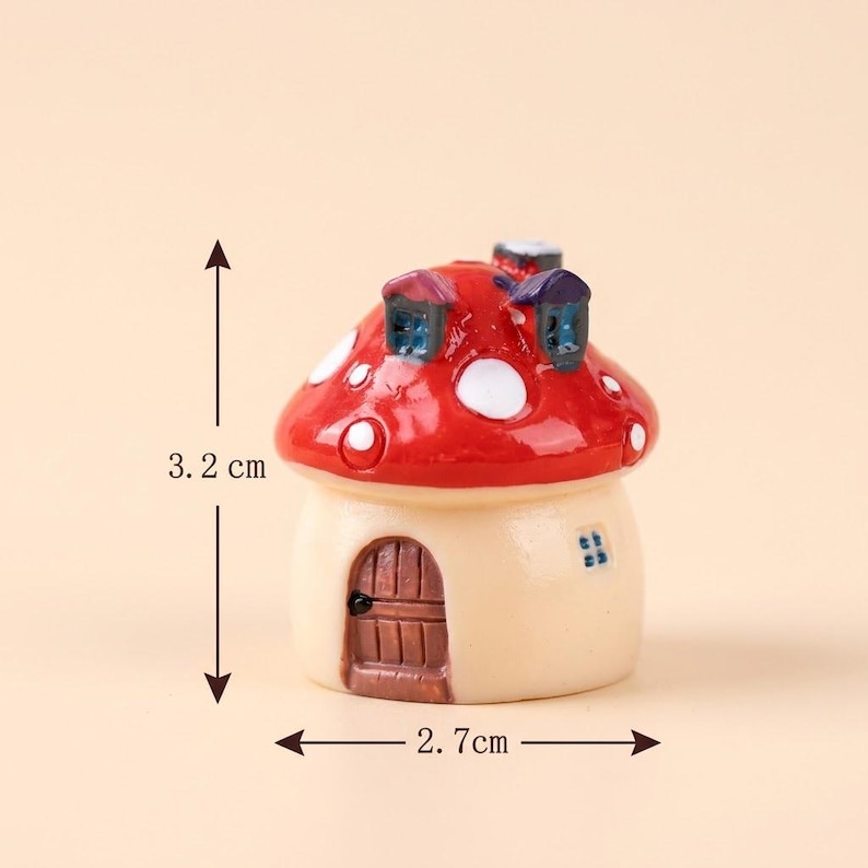 May include: A miniature mushroom-shaped house figurine with a glossy red cap featuring white spots and two small dormer windows. The base is cream-colored with a brown arched door and a small window. It measures 3.2 cm in height and 2.7 cm in width.