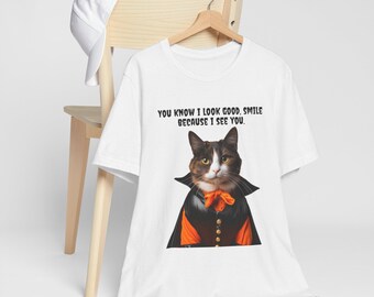 May include: White t-shirt featuring a cat dressed in a vampire costume with an orange bow tie. The shirt has the text "YOU KNOW I LOOK GOOD. SMILE BECAUSE I SEE YOU."