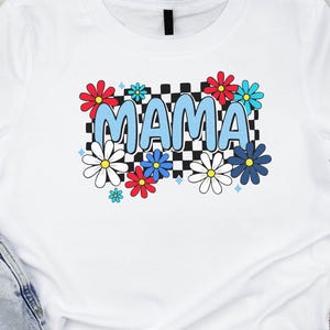 May include: White t-shirt with a retro floral design. The word "MAMA" is in light blue, surrounded by red, blue, and white flowers. A black and white checkered pattern is behind the word "MAMA".