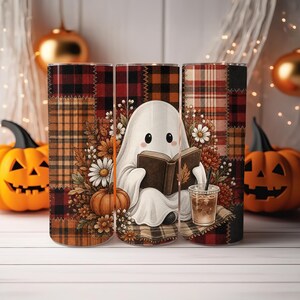 May include: A cylindrical tumbler featuring a patchwork plaid pattern in red, orange, and black. The design displays a white ghost reading a brown book, surrounded by autumn flowers, a small pumpkin, and a clear plastic cup with a straw.
