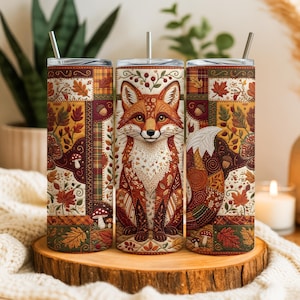 May include: A set of three stainless steel insulated tumblers with lids and straws. Each tumbler features a detailed illustration of a fox with autumn-themed patchwork patterns in shades of orange, brown, and cream. The design includes leaves, mushrooms, and berries.