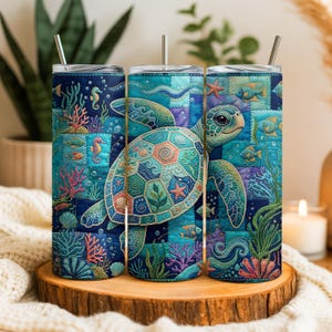May include: Three stainless steel tumblers with a sea turtle design. The tumblers feature a patchwork design with a large sea turtle in the center, surrounded by coral, fish, and seahorses. Each tumbler has a silver straw.