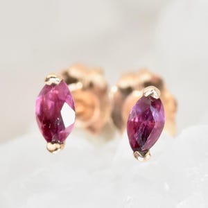 May include: A pair of small, rose gold earrings with a marquise-shaped pink gemstone in each earring.