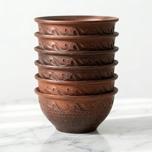 May include: A stack of six brown ceramic bowls. Each bowl features a wavy, carved design around the rim. The bowls are stacked, with the bottom bowl slightly larger. The bowls have a rustic, earthy appearance. The bowls are made of ceramic.