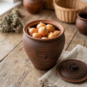 May include: A brown ceramic onion store with a lid, filled with small onions. The store has a floral design carved into the side. The lid is off to the side, and the store sits on a wooden surface.
