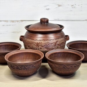 K&ouml;nnte beinhalten: Ein Set aus braunen Keramik-Servierschalen und einem Topf mit Deckel. Die Schalen und der Topf haben ein rustikales Aussehen mit geschnitzten Blumen- und Blattmustern. Das Set enth&auml;lt einen gro&szlig;en Topf mit Griffen und vier kleinere Schalen.