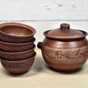 K&ouml;nnte beinhalten: Ein Set aus handgefertigten braunen Keramikschalen und einem passenden Topf mit Deckel. Die Schalen sind gestapelt, und der Topf hat ein dekoratives Blumenmuster. Die T&ouml;pferwaren haben eine rustikale, erdige &Auml;sthetik.