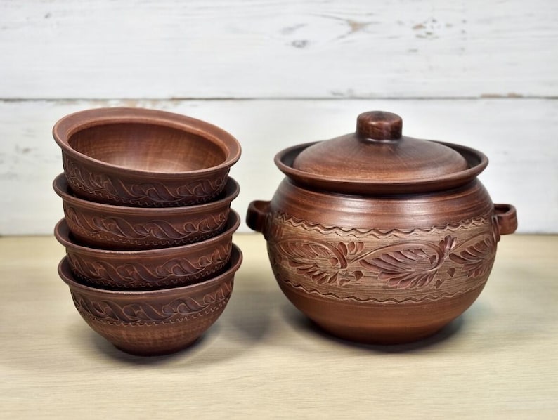 K&ouml;nnte beinhalten: Ein Set aus handgefertigten braunen Keramikschalen und einem passenden Topf mit Deckel. Die Schalen sind gestapelt, und der Topf hat ein dekoratives Blumenmuster. Die T&ouml;pferwaren haben eine rustikale, erdige &Auml;sthetik.