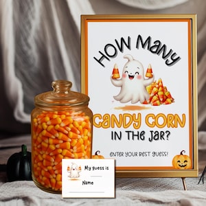 May include: A clear glass jar filled with orange, yellow, and white candy corn next to a framed sign that reads How Many Candy Corn In The Jar? Enter Your Best Guess! with a ghost illustration and a small matching guess card with a ghost graphic.