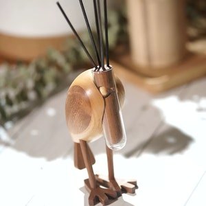 Könnte beinhalten: Holzskulptur eines Vogels mit einem Glasrohr für Räucherstäbchen. Der Vogel ist braun und hat einen langen Schnabel. Die Räucherstäbchen sind schwarz.